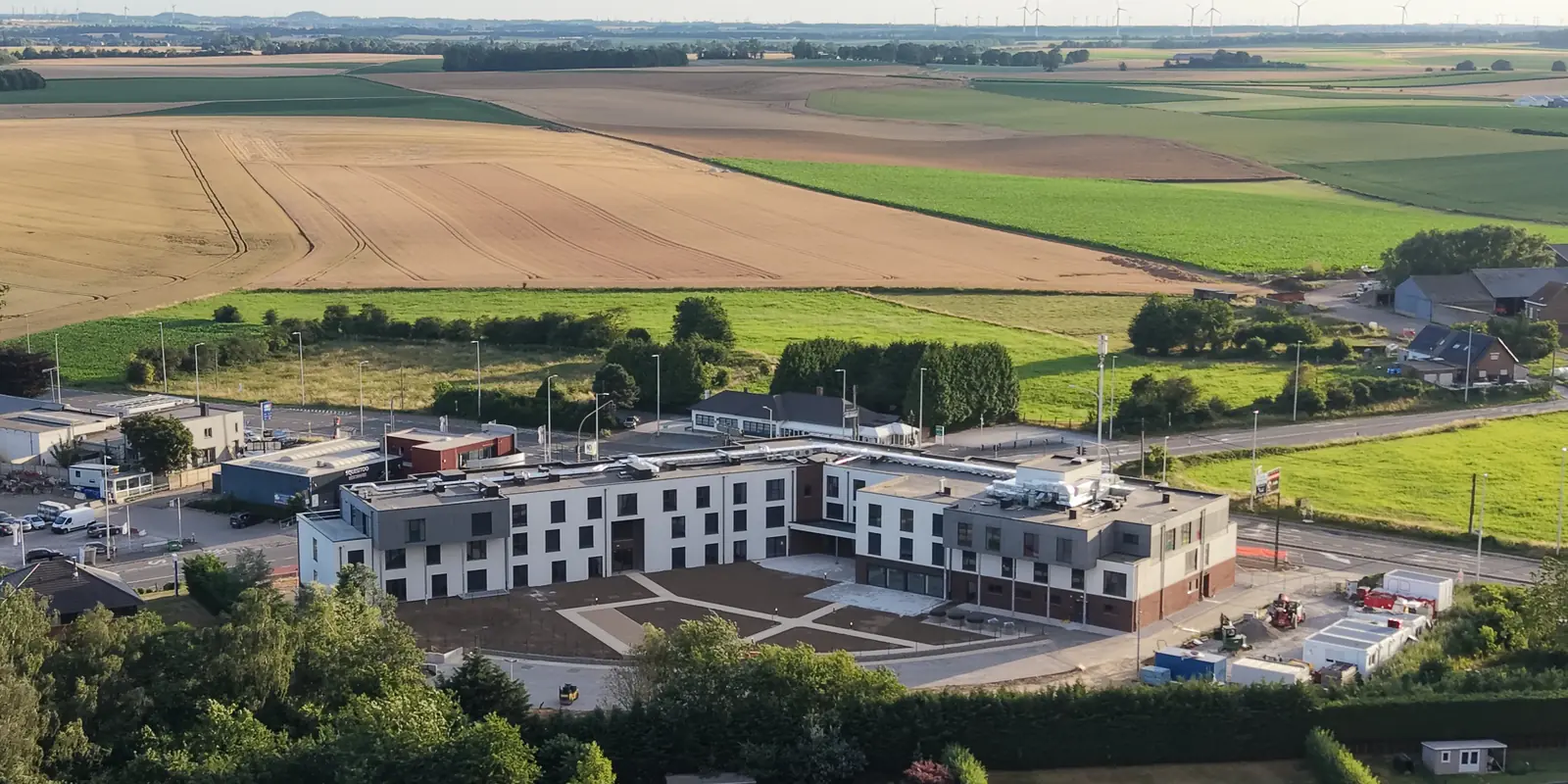 Vue aérienne par drone d'une résidence neuve en fin de chantier, abords en cours d'aménagement, campagne wallonne et éoliennes en arrière-plan